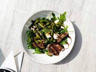 Top view of beef roasted meat with balsamic vinegar, green beans, and arugula on a white plate....