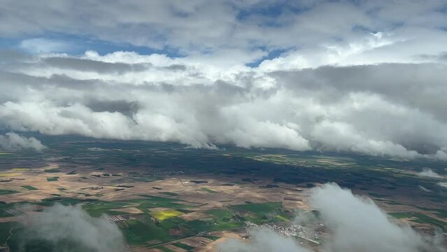 Aerial view from a cockpit of a cludy sky over green and brown fields in central Spain.