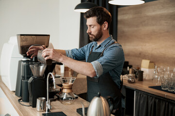 Handsome barista wearing apron grinds coffee beans in coffeemachine