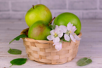 Ripe green apples in a basket, on a white wooden table.
