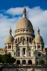 Front view of the Basilica of the Sacré-Coeur in the Parisian district of Montmartre on a sunny day with white clouds in the sky.