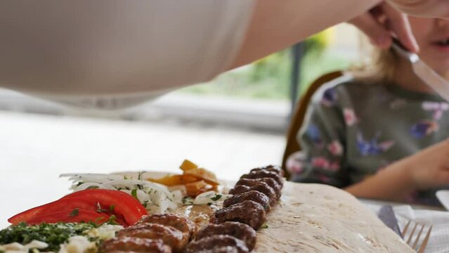 mom and little daughter eat lula kebab with fresh vegetables. The woman gave the child fried potatoes, but the daughter refused. Outdoor lunch in the park