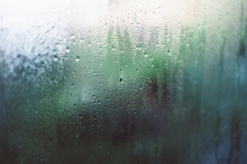 water droplets of humidity condensation on window glass seen from indoor with backyard bokeh in the background
