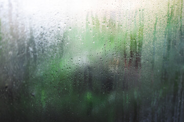 water droplets of humidity condensation on window glass seen from indoor with backyard bokeh in the...