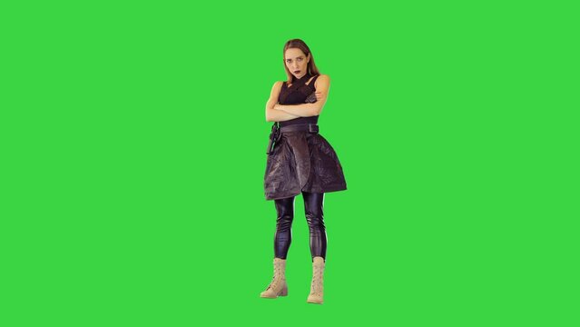 Game-character girl with a gun on belt stands folding her arms in threatening manner on a Green Screen, Chroma Key.