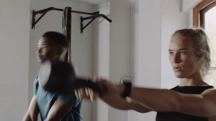 Black young adult male swinging kettlebells with diverse group of friends at an indoor fitness gym. - Powered by Adobe