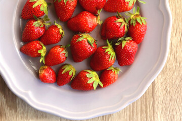 Lilac plate full of fresh strawberries on wooden table. Flat lay.
