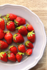 Lilac plate full of fresh strawberries on wooden table. Flat lay.