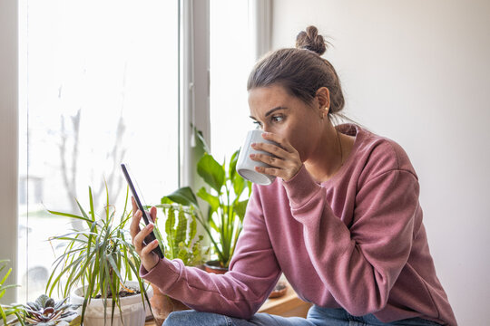 Young woman sitting by window, looking at digital tablet