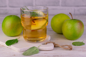 Apple juice from green apples in a glass on a white wooden board.
