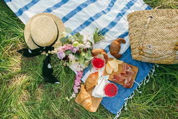 Picnic in the Park on the green grass with berry, croissants, juice, bouquet, hat. Picnic blanket. Summer holiday