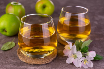 Two glasses with fresh apple juice on a gray background.

