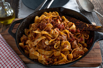 Braised chicken meat with tomato herb sauce and pasta in a rustic cast iron pan
