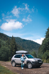 Girl standing near suv car at the Charpatians mountain. Vertical photo. summer day. Road trip, vacation and travel concept. Roff rack box.