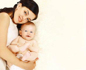 Portrait of happy smiling young mother and cute baby lying on the bed at home together, top view, blank copy space for advertising text