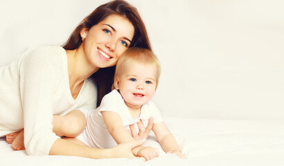 Fototapeta na wymiar Portrait of happy smiling young mother and cute baby lying on the bed at home together