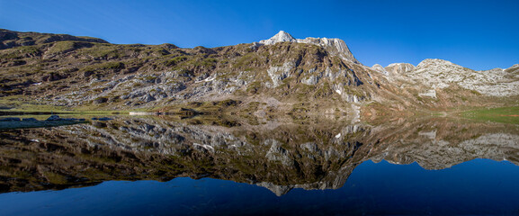 Fototapeta na wymiar Cerveriz Lake in the Somiedo Natural Park in Asturias, Spain. A dream environment where the mountains are reflected in the lake like a mirror. Panoramic photo of nature in its purest state, ideal for 