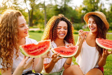 Three young woman  camping on the grass, eating watermelon, laughing. People, lifestyle, travel, nature and vacations concept. Summer concept.
