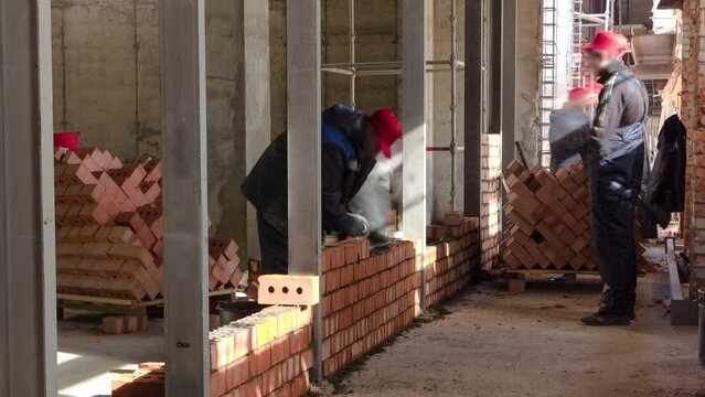 Bricklayers laying bricks to make a walls timelapse and welders weld fittings in reinforcement. Professional construction worker laying red bricks and building inside in industrial site.