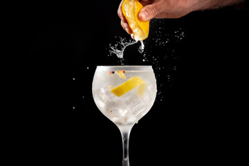 Squeezing a lemon into a glass of gin tonic on black background - obrazy, fototapety, plakaty