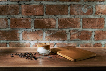 A Glass of Dirty coffee by espresso shot topped over cold fresh milk create a gradient layer in the morning over a red bricks wall background and coffee beans on a wooden Cafe table. For Copy Space