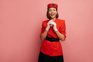 Happy young caucasian brunette girl is pleasantly surprised with mouth open while standing on pink background. Beauty model wears stylish red jacket. Elegant, fashion trend concept