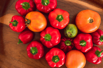 freshly picked mini capsicums and tomatoes with vibrant red and orange tones on wooden tray, simple ingredients concept