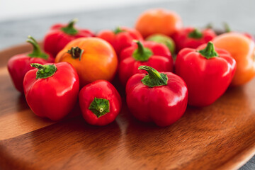 freshly picked mini capsicums and tomatoes with vibrant red and orange tones on wooden tray, simple ingredients concept