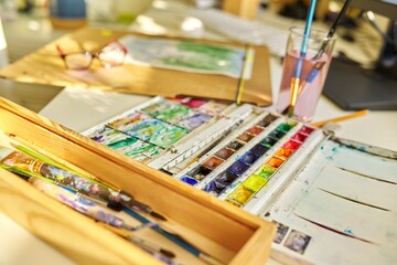 Watercolor drawing, glasses, watercolors in a box, brushes on the table, nobody