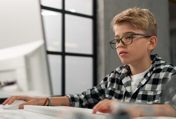 Naklejka na ściany i meble Schoolboy using computer in classroom at school