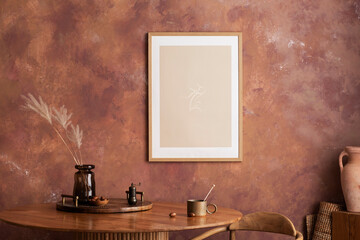Stylish boho vintage dining room interior with poster mock up. Round table with wooden tray, vase with dried flowers and cup. Brown wall and rattan lamp. Mock up poster. Template.