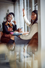 Two hipster multiracial female students sitting in a cafe making an order while working on the assignment.
