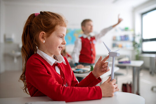Schoolgirl holding wind turbine and learning about eco-friendly renewable sources of energy in classroom at school