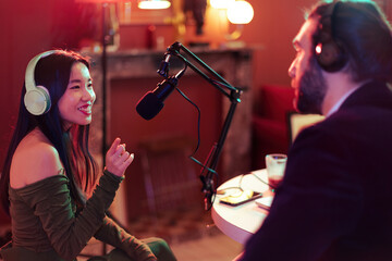 smiling asian woman interviewing a man speaking on the mic at a podcast