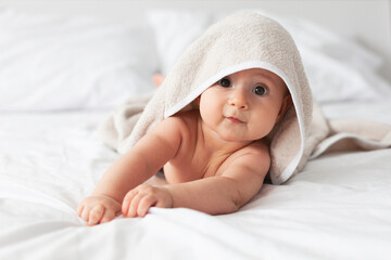 Fototapeta na wymiar Happy laughing baby wearing biege towel on parents bed after bath or shower.