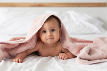 Fototapeta na wymiar Happy laughing baby wearing pink hooded towel on parents bed after bath or shower.