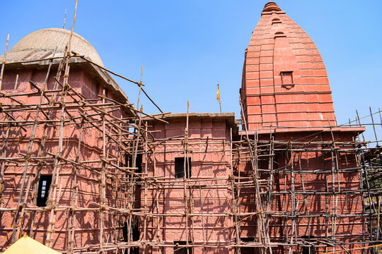Stock photo of architectural and renovation site of old hindu temple,bamboo scaffolding on red color painted temple building . Picture captured under bright sunlight at Naikba Mandir patan, satara.