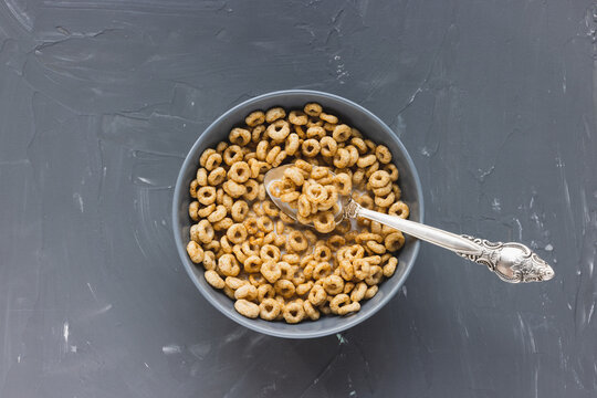 Delicious Honey Cheerios Cereal In A Bowl With Milk And Spoon On Gray Background. Top View, Flat Lay, Copy Space. Breakfast Concept