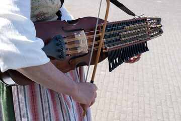 Woman in Swedish traditional costume plays folk music on a modern nyckelharpa in a close-up with focus on the bow, strings and bow