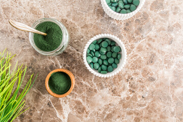 top view of glass jars with green spirulina superfood tablets and powder on a marble table. alternative to medicine.