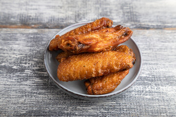 fried chicken wings on a wooden plate on a gray. Side view.