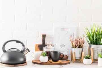 front view of a marble countertop with kitchen utensils and houseplants in modern pots. white brick background of the wall. a copy of the space.