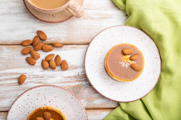 Sweet tartlets with almonds and caramel cream with cup of coffee on a white wooden background. flat lay, close up.