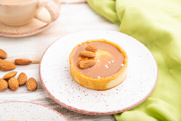 Sweet tartlets with almonds and caramel cream with cup of coffee on a white wooden background. side view, selective focus.