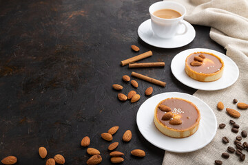 Obraz na płótnie Canvas Sweet tartlets with almonds and caramel cream with cup of coffee on a black concrete background. Side view, copy space.