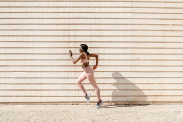 Side view of a fit young African American woman running forward against the backdrop of the city wall . Concept of sports activity and health, copy space