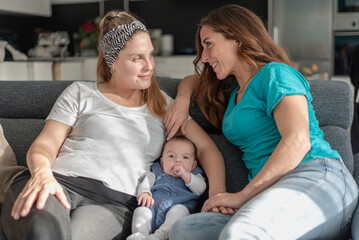 a young lesbian couple sitting on the couch with their baby-gay parents, gay marriage and adoption concept