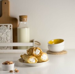 Cakes with white cream on a white plate. On the white table there is milk, peanuts.