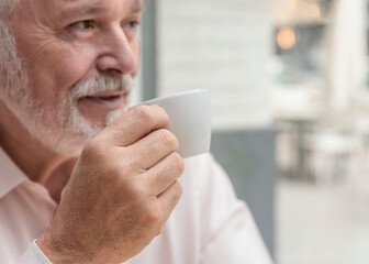 the close-up of an out-of-focus older man holding a cup of coffee or tea