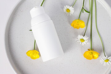 White cosmetic container on marble plate with flowers, mockup